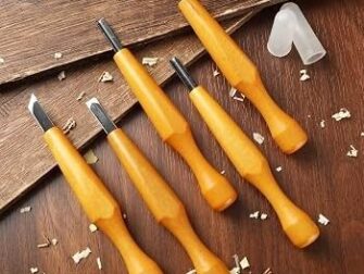 Mehrere Linolschnittmesser mit orangefarbenen Griffen auf Holz